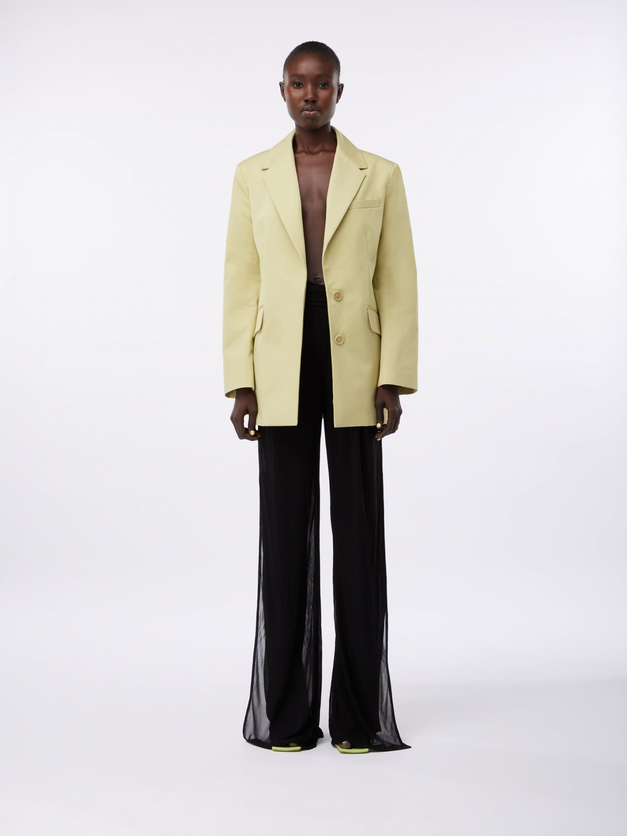 model wearing a pale olive square blazer and draped trousers with twist detail